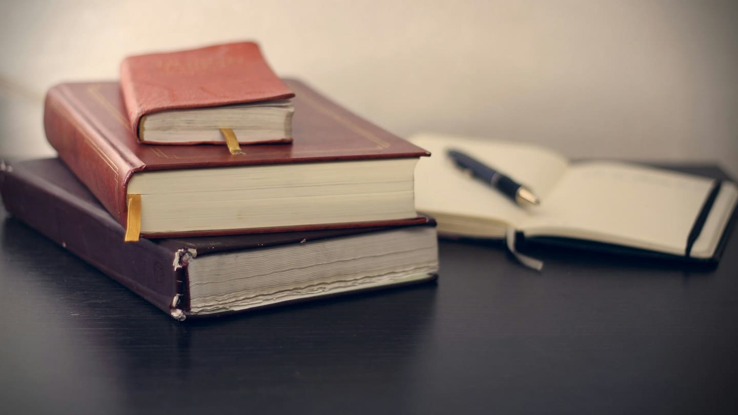 Tumpukan buku hukum bersampul kulit dan buku catatan di atas meja